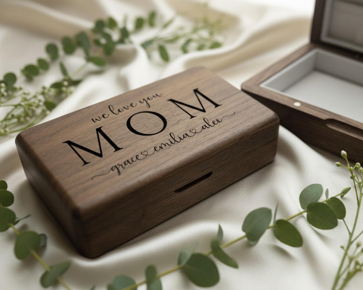A wooden box with the text "we love you Mom Grace & Alex" engraved on it, surrounded by greenery and a white cloth.