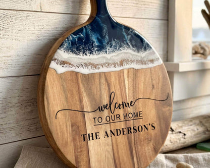 A wooden cutting board with a blue and white wave design on it, and the text "Welcome to our home" printed on it.