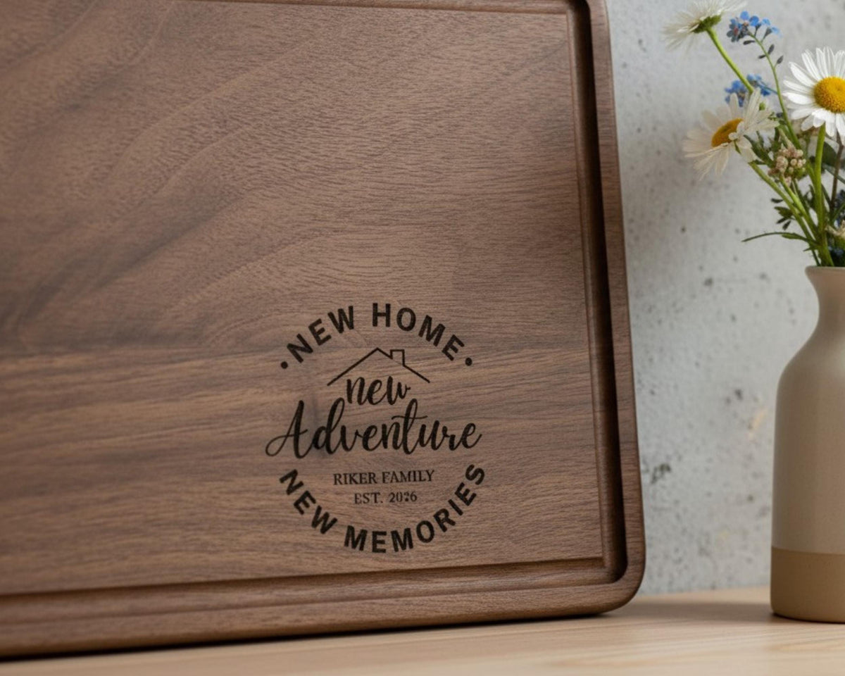A wooden cutting board with a decorative design and text that says "NEW HOME. NEW ADVENTURE. RIKER FAMILY. EST. 2028" is placed next to a vase with flowers on a table.