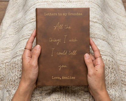 A person's hands holding a brown leather-bound book titled "Letters to my Grandma All the things I wish I could tell you."