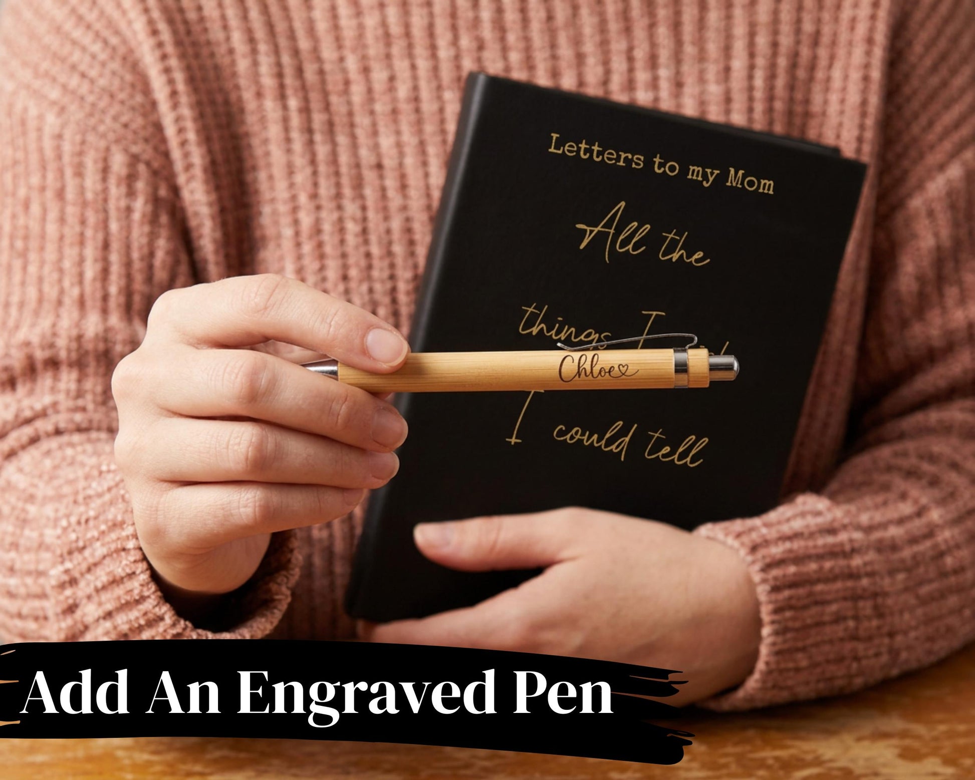 A person is holding a black notebook with the words "Letters to my Mom" written on it, and a wooden pen with the words "All the things I could tell" engraved on it.