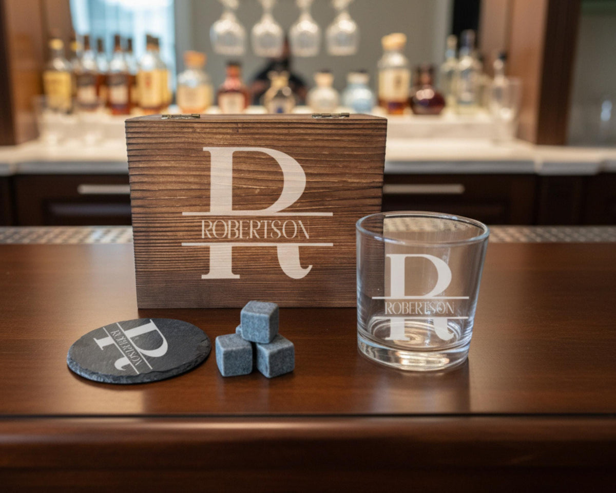 a wooden box with a personalized monogrammed name on it, a glass with a personalized monogrammed name, and some gray rocks on a wooden surface.