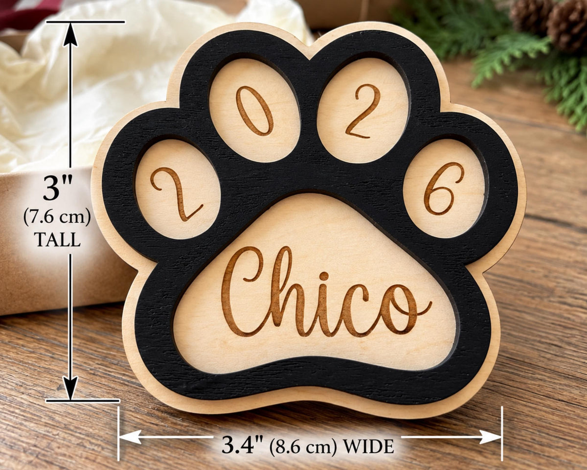 A wooden paw print-shaped object with the name "Chico" engraved on it, placed on a wooden surface.