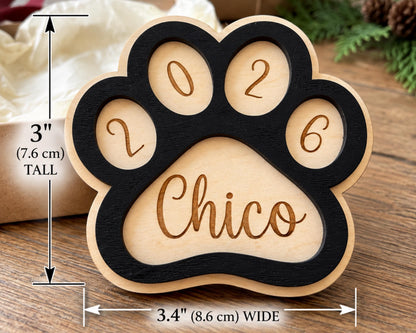 A wooden paw print-shaped object with the name "Chico" engraved on it, placed on a wooden surface.
