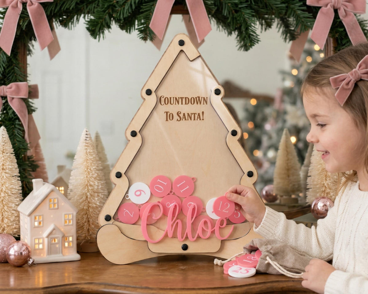 A young girl is playing with a pink and white countdown timer shaped like a Christmas tree, surrounded by holiday decorations and ornaments.