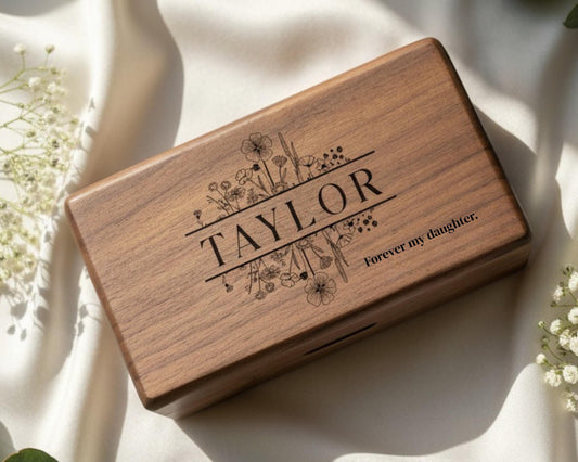 A wooden box with the name "TAYLOR" engraved on it, surrounded by floral designs.