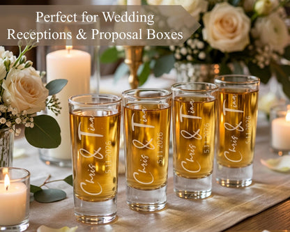 a table with four shot glasses filled with a golden liquid, likely champagne or a similar beverage, arranged in a row. The shot glasses have personalized text engraved on them, suggesting they are intended for a wedding reception or similar event.