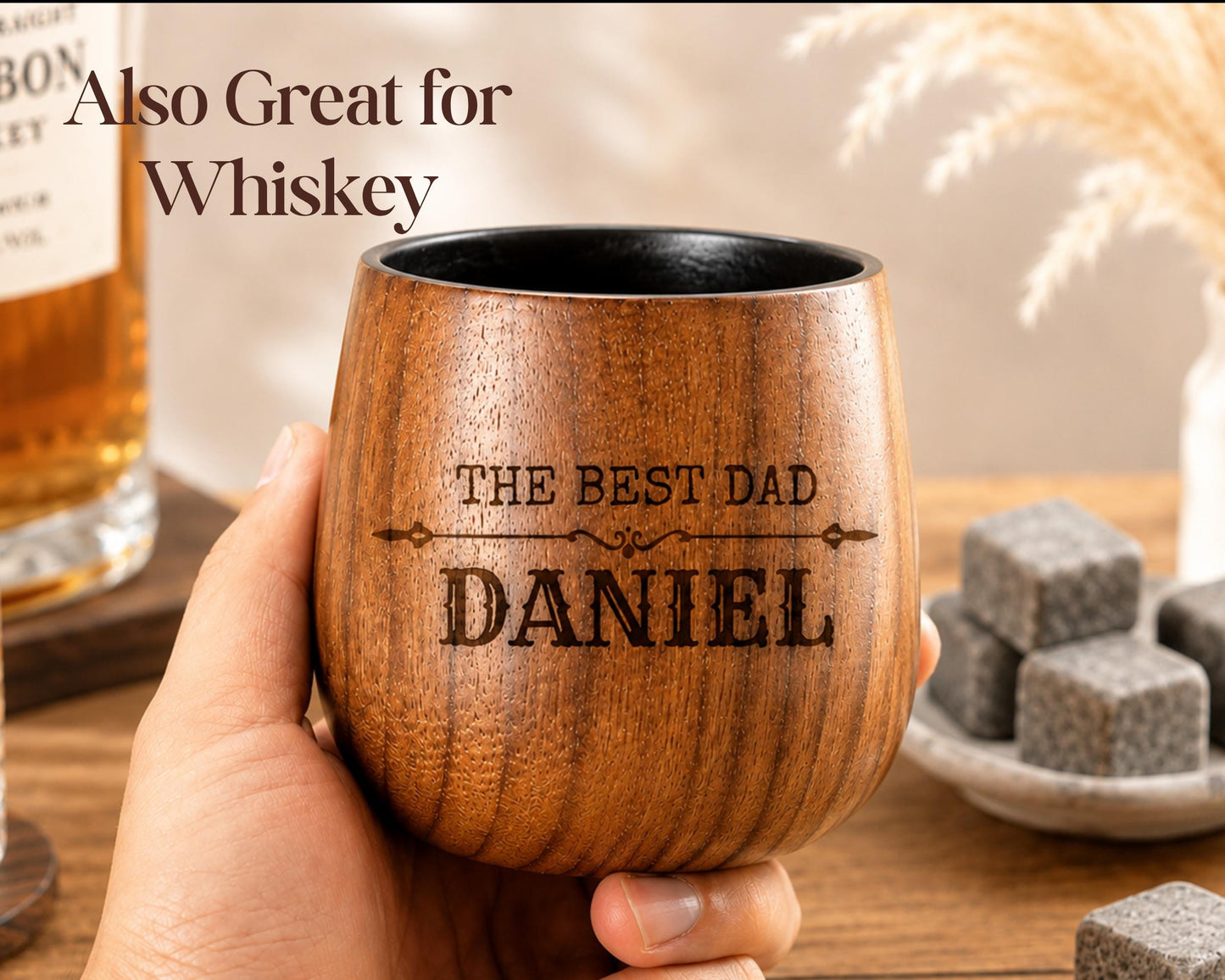 A wooden mug with the text "The best dad Daniel" engraved on it, held in a person's hand.