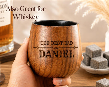 A wooden mug with the text "The best dad Daniel" engraved on it, held in a person's hand.