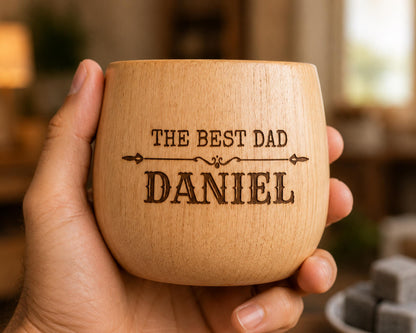 A wooden mug being held in a hand, with the text "THE BEST DAD DANIEL" engraved on it.