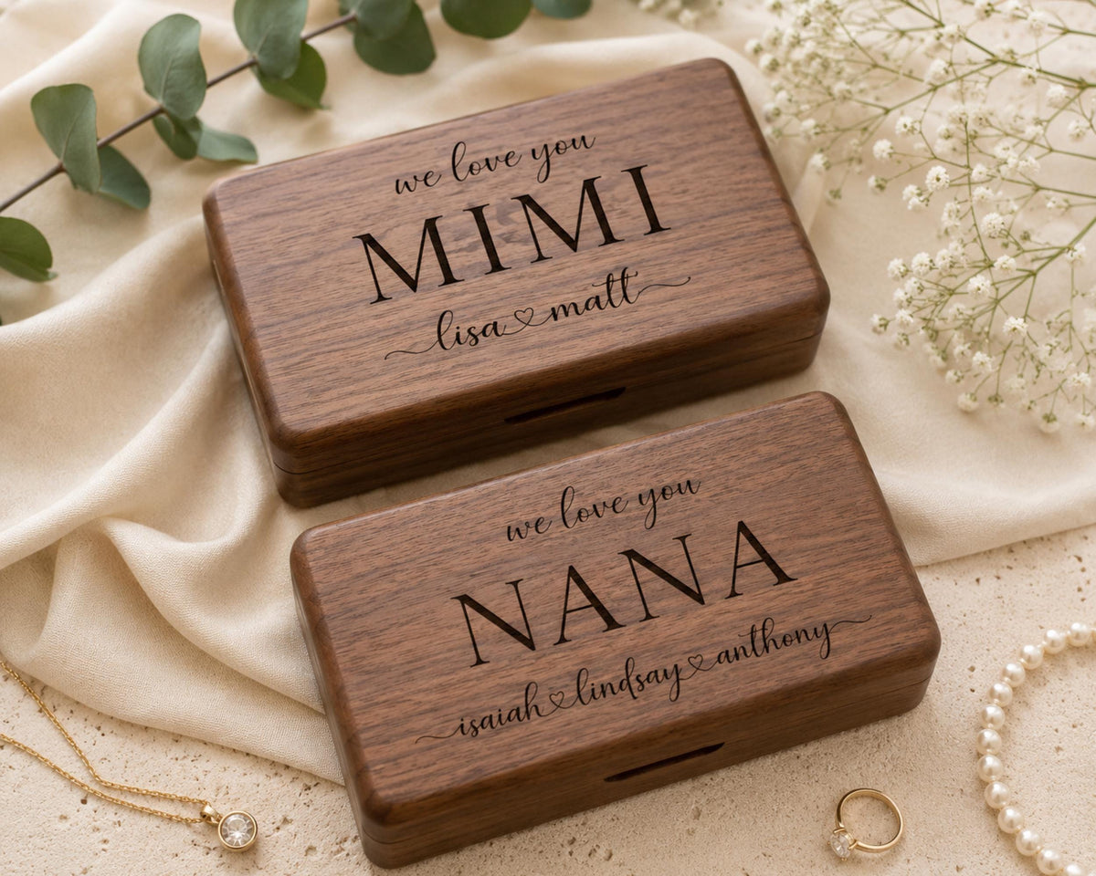 Two wooden boxes with personalized messages, placed on a beige cloth and surrounded by pearls and greenery.