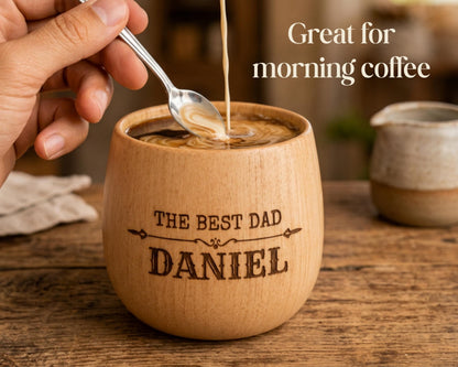 A hand is pouring coffee into a wooden mug with the text "THE BEST DAD DANIEL" engraved on it.
