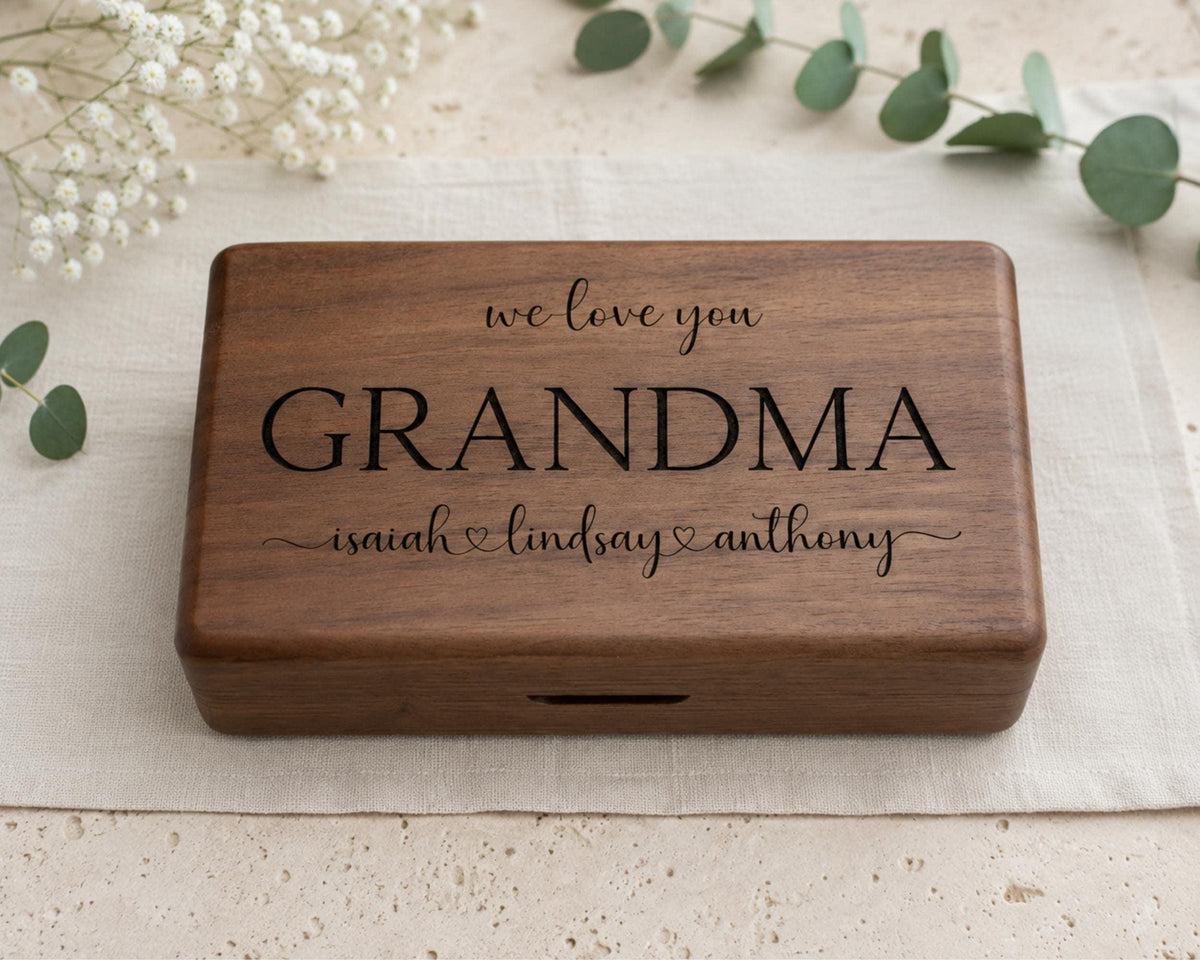 A wooden box with the inscription "we love you GRANDMA Isaiah & Lindsay Anthony" engraved on it, placed on a beige cloth.