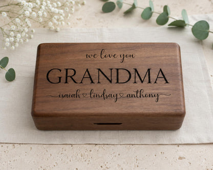 A wooden box with the inscription "we love you GRANDMA Isaiah & Lindsay Anthony" engraved on it, placed on a beige cloth.