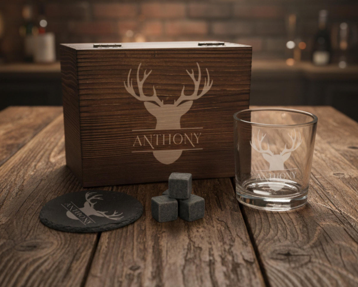 a wooden box with a deer head logo, a glass, and some gray rocks on a wooden table.