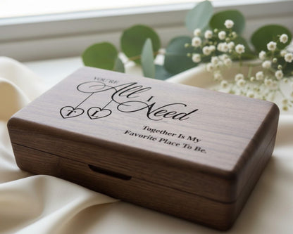 A wooden box with a decorative design and text on it, placed on a white cloth near some greenery.