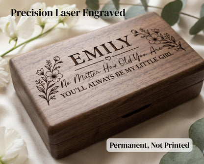 A wooden box with a personalized engraved message on it, surrounded by white flowers.