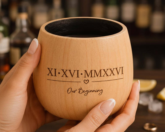 A person's hand holding a wooden mug with the text "XI: XVI: MMXXVI: Our Beginning" printed on it.