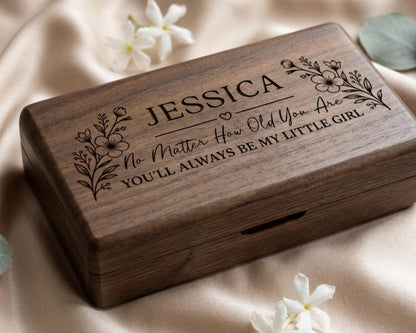 A wooden box with the name "JESSICA" engraved on it, surrounded by white flowers.