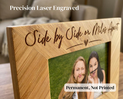 A wooden picture frame with a photo of two women making silly faces, and the frame has the text "Side by Side or Miles Apart" engraved on it.