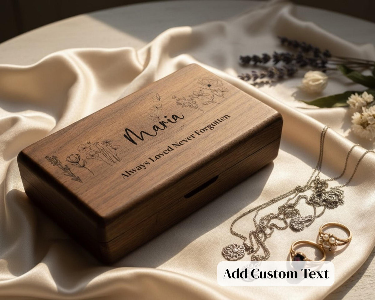 A wooden box with a personalized message engraved on it, surrounded by jewelry and flowers on a white cloth.