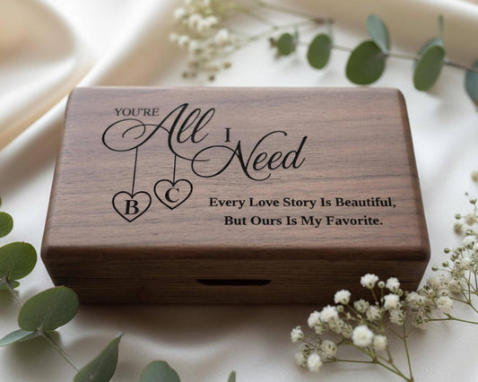 A wooden box with a personalized message engraved on it, surrounded by white flowers and greenery.