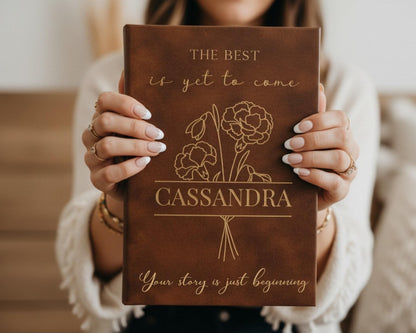 A person is holding a brown leather-bound book titled "The Best is yet to Come" by Cassandra, with the book's cover featuring a floral design.