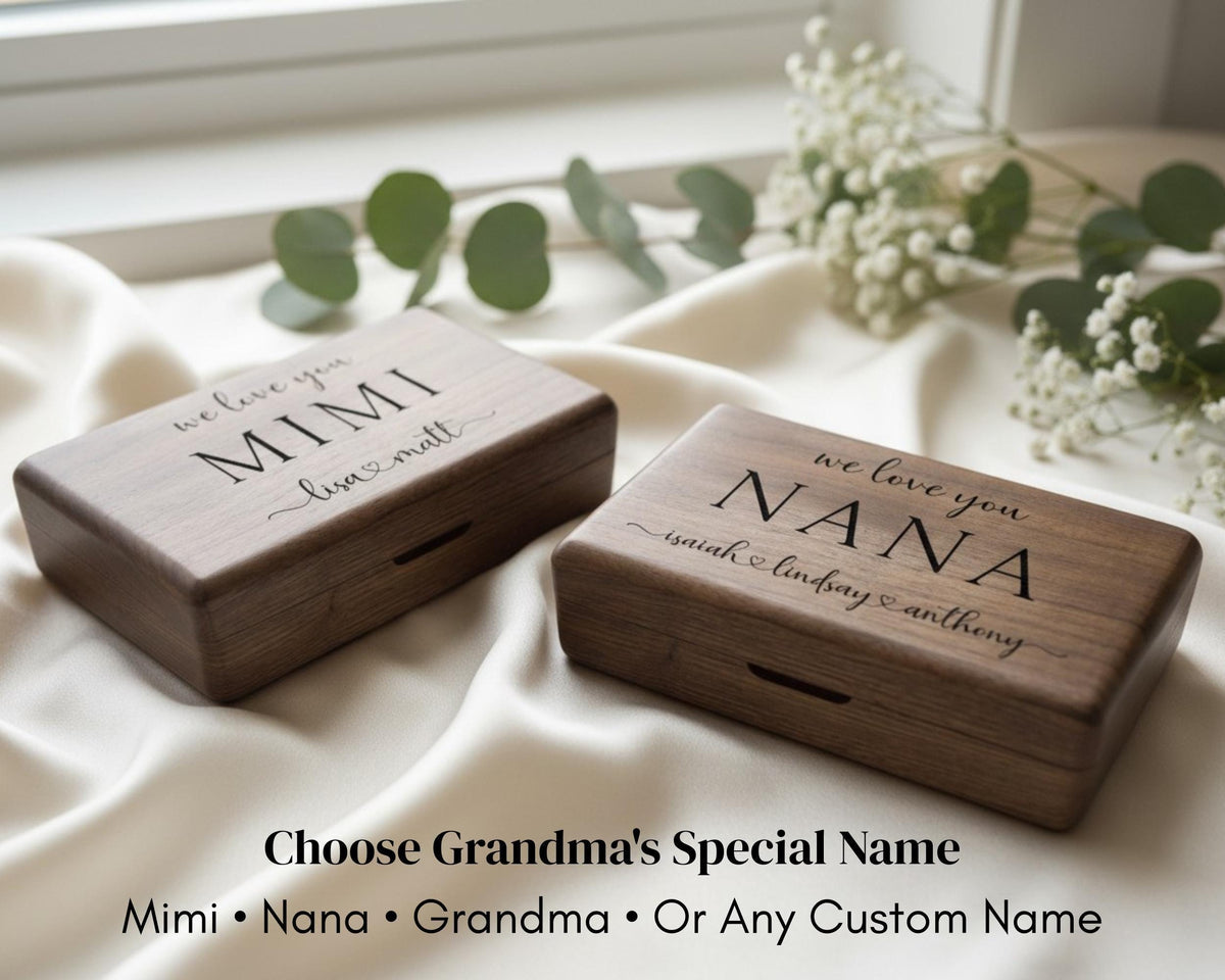 Two wooden boxes with personalized names on them, placed on a white cloth with greenery in the background.