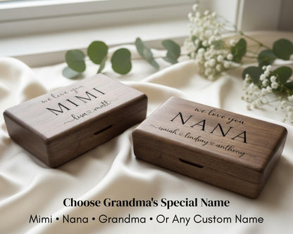 Two wooden boxes with personalized names on them, placed on a white cloth with greenery in the background.