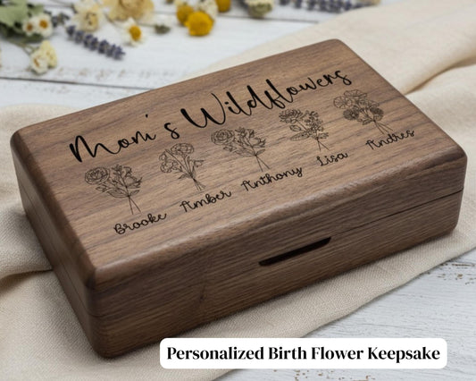 A wooden box with the text "Moni's Wildflowers" engraved on it, along with illustrations of different flowers. The box appears to be a personalized birth flower keepsake.