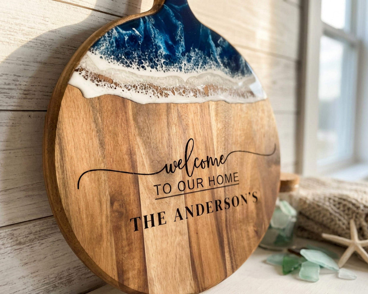 A wooden cutting board with a wave-like design and the text "Welcome to our Home" printed on it.