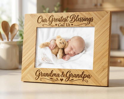 A wooden picture frame with a photo of a sleeping baby and a teddy bear inside. The frame has a message that reads "Our Greatest Blessings Call Us Grandma & Grandpa".