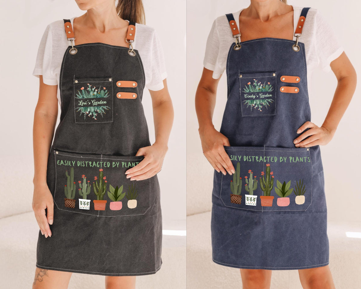 two women wearing aprons with a plant-themed design. The aprons have pockets with illustrations of potted plants and the text "Easily distracted by plants" printed on them.
