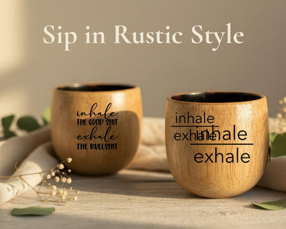 two wooden cups with humorous sayings on them, placed on a wooden surface with some greenery in the background.