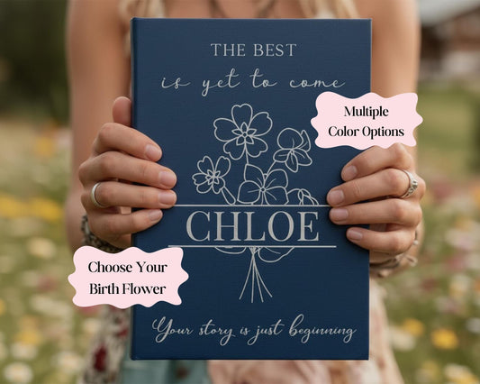 A person is holding a blue book with the title "The Best is yet to Come" and the name " Chloe" printed on it. The book also has a section titled "Choose Your Birth Flower" and a section titled "Your story is just beginning".