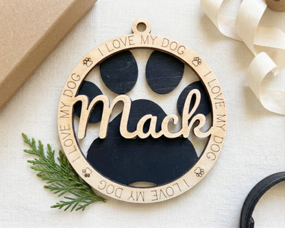 A wooden ornament with the name "Mac" engraved on it, surrounded by a circular frame with paw prints and the phrase "I LOVE MY DOG" written around the edges.