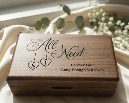 A wooden box with a decorative design and text on it, placed on a white cloth near some greenery.