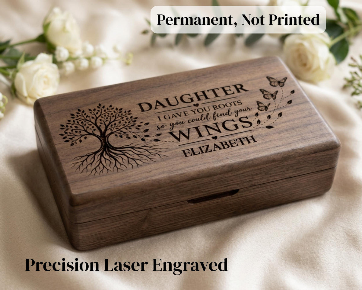 A wooden box with a tree design and text engraved on it, placed on a white cloth with white roses in the background.