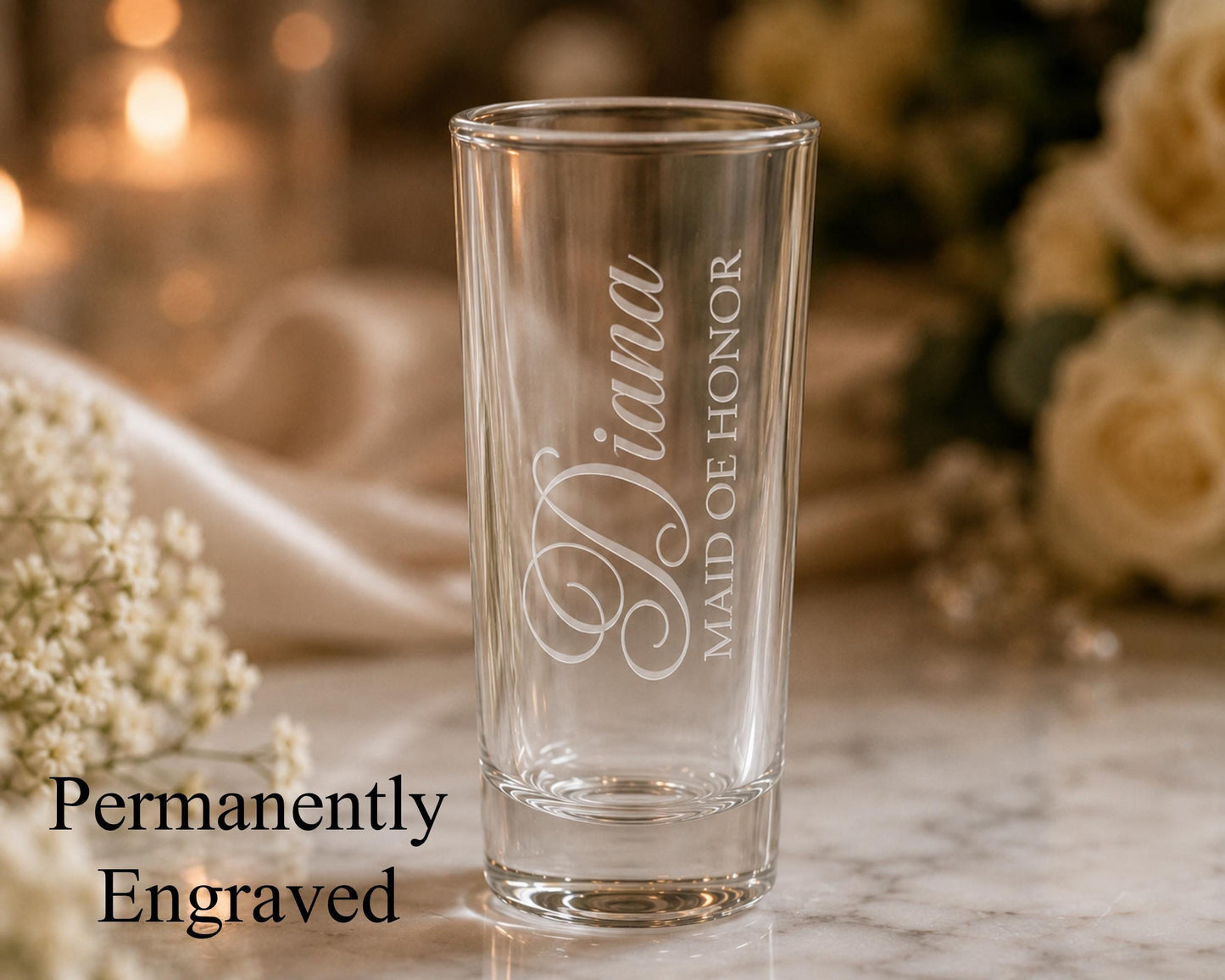 A glass with the engraved name "Diana" on it, placed on a marble surface with a blurred background of flowers.