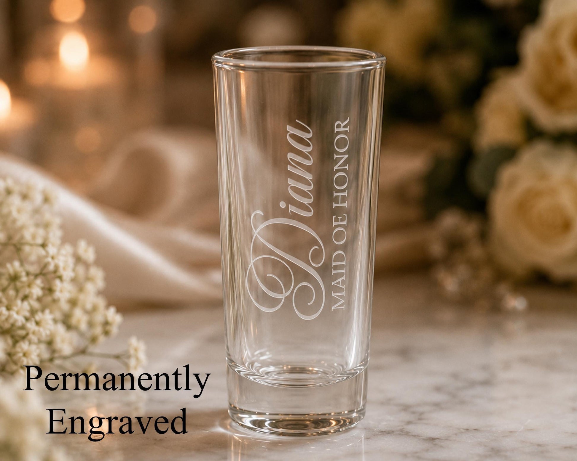 A glass with the engraved name "Diana" on it, placed on a marble surface with a blurred background of flowers.