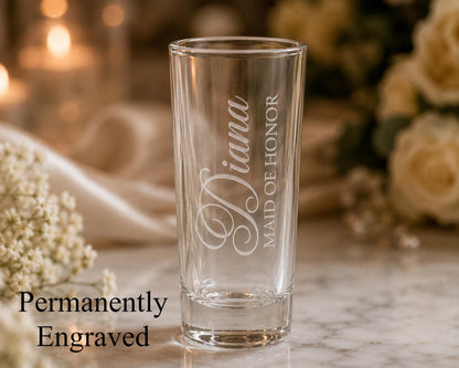A glass with the engraved name "Diana" on it, placed on a marble surface with a blurred background of flowers.