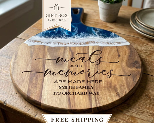 a wooden cutting board with a decorative design and text on it. The cutting board is placed on a wooden table, and there is a potted plant in the background.