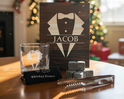 a set of whiskey-related items, including a glass, whiskey stones, and a wooden box with a tuxedo design.