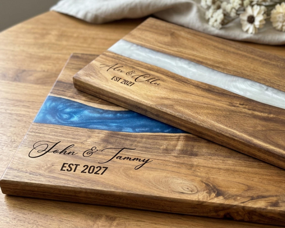 Two personalized acacia cutting boards with blue pearl resin rivers and engraved couple names
