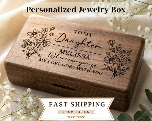 A wooden jewelry box with a personalized message engraved on it, placed on a white cloth with small white flowers.