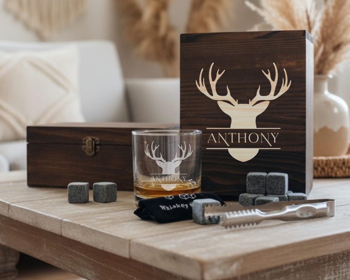 a set of whiskey accessories, including a wooden box, a glass, and a set of whiskey stones, arranged on a wooden table.