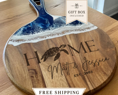 A wooden cutting board with a blue and white wave design and the text "HOME Matt & Jessica EST. 2003" engraved on it.