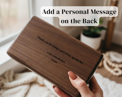 A person's hand holding a wooden box with a personal message engraved on it, placed near a window.