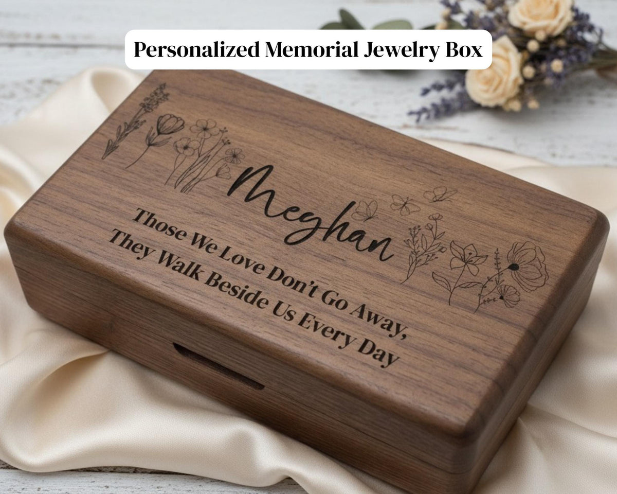 A wooden jewelry box with the name "Meghan" engraved on it, along with a message about loving and not going away. The box is placed on a white cloth, and there are some flowers in the background.